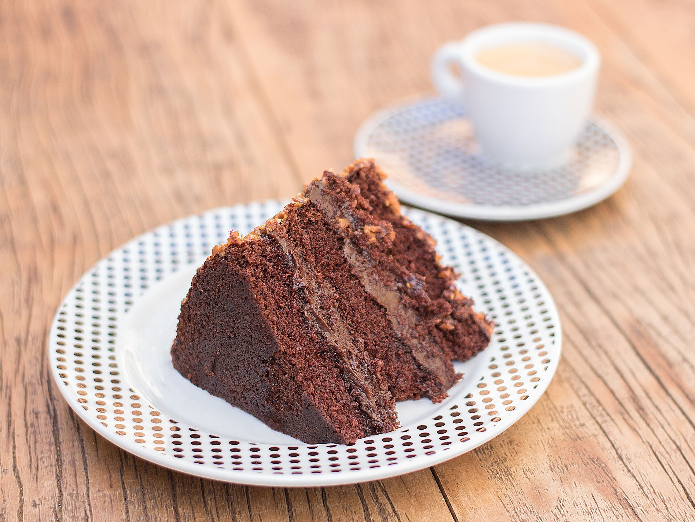 Delicious slice of chocolate cake served with coffee on a rustic wooden table, perfect for dessert lovers.